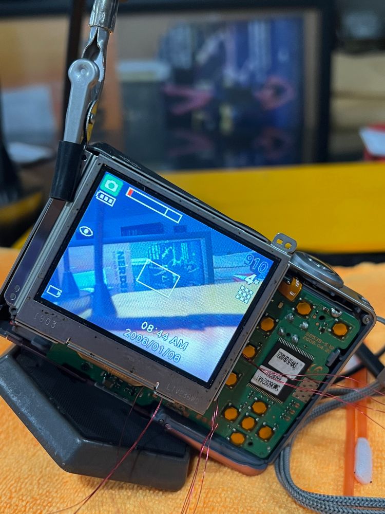 Its the still open back of the Samsung digimax s500 but with a tripod shoe screwed in to prop it up. A bendy helping hand is holding the connected LCD so that I can still maneuver the 12 wires coming off the resistor networks. The camera is pointing at a large picture frame containing random posters people have wrapped vinyl records in to ship to me