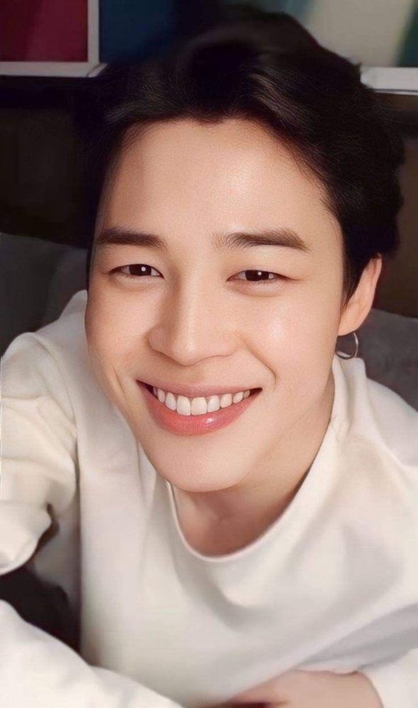 Goegeous close-up of Jimin, who’s wearing a long sleeve white shirt, is leaning forward with a dimpled smile