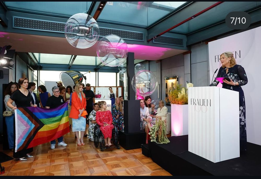 Julia Klöckner hält eine Rede. In der ersten Reihe halten mehrere Leute eine Prideflagge.