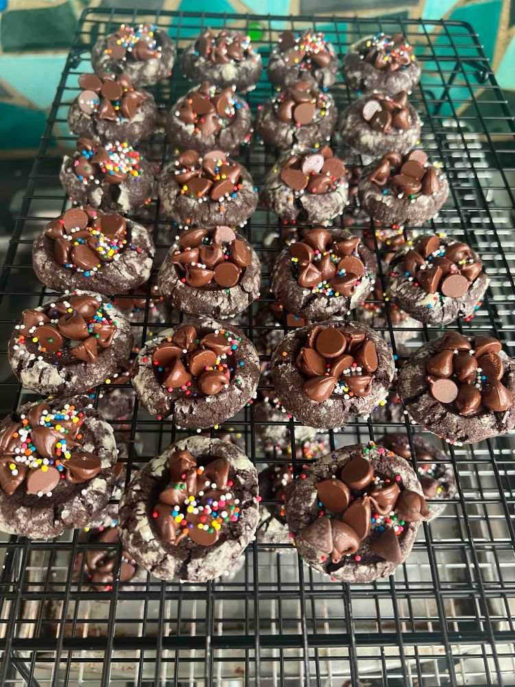 Chocolate cookies on a rack cooling - they have thumbprint depressions on top that are filled with chocolate chips sprinkled with teeny tiny multi-colored balls of sugar.
