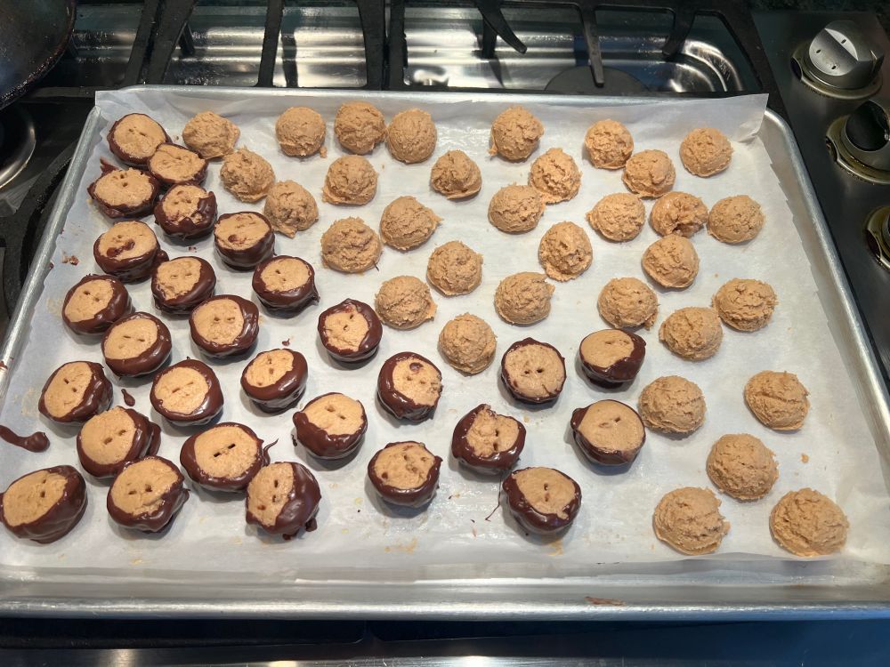 Halfway through the chocolate dipping process of the peanut butter cookie balls. The skewer prong marks (used in dipping) are still visible on the top.