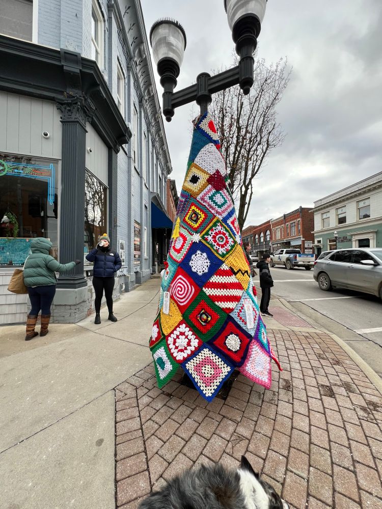 Two women and a dog standing beside a Christmas tree decorated with crocheted panels