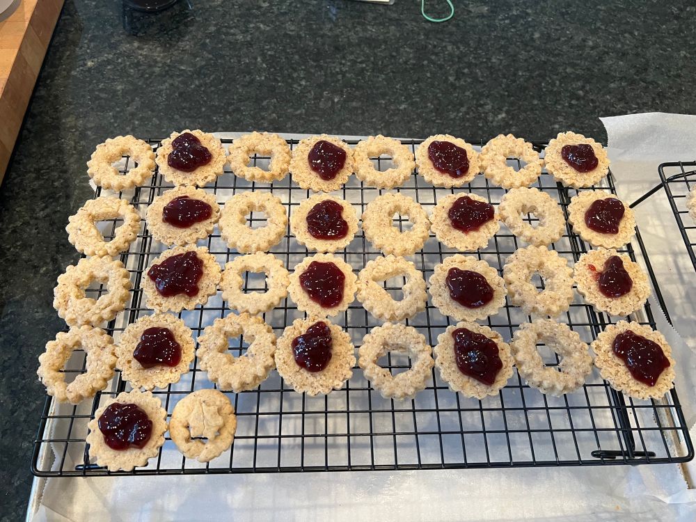 Linzer cookie bases with tea spoon of seedless raspberry jam in top. Cut out tops are beside their respective base.