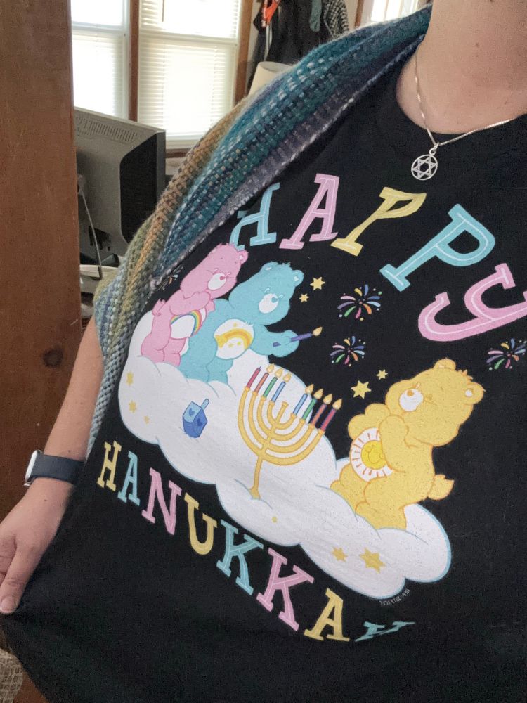 Black tee with 3 Care Bears on a cloud lighting a menorah on the 8th night.