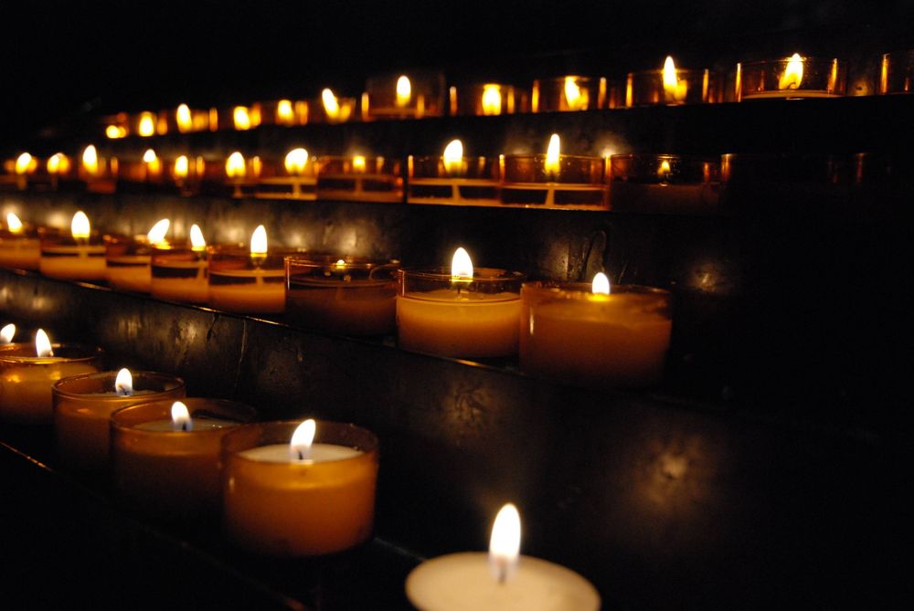 A lot of little candles as you see in a church for remembering lost ones. They are burning in the complete darkness.