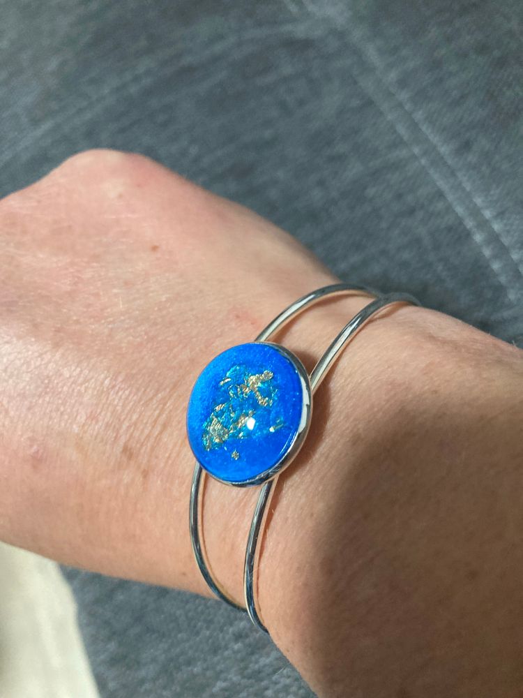 Ein silberner Armreif mit hellblauen Stein und Goldsprengel darin 