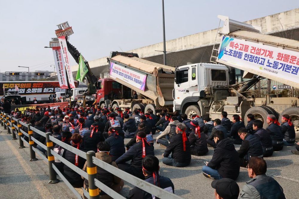 Protestors sitting in rows in the road, next to parked lorries