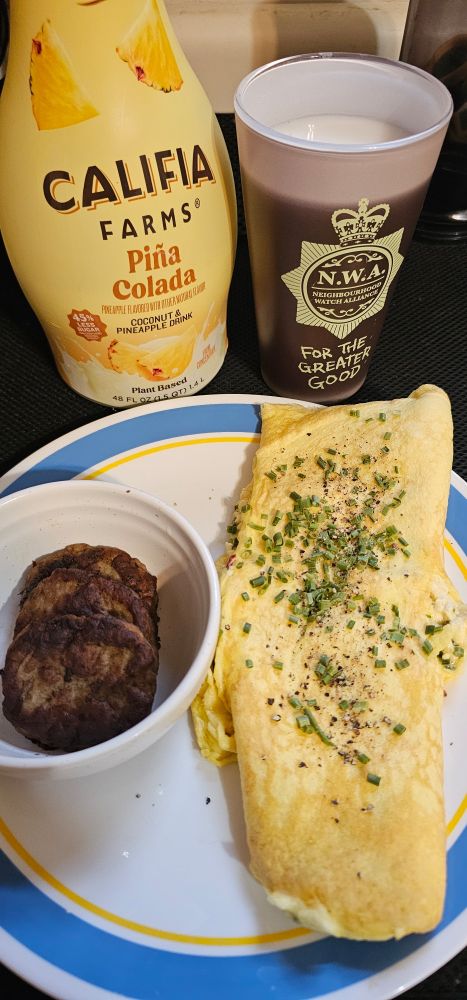Breakfast of an omelet with feta and chives, sausage patties, and a pina colada juice