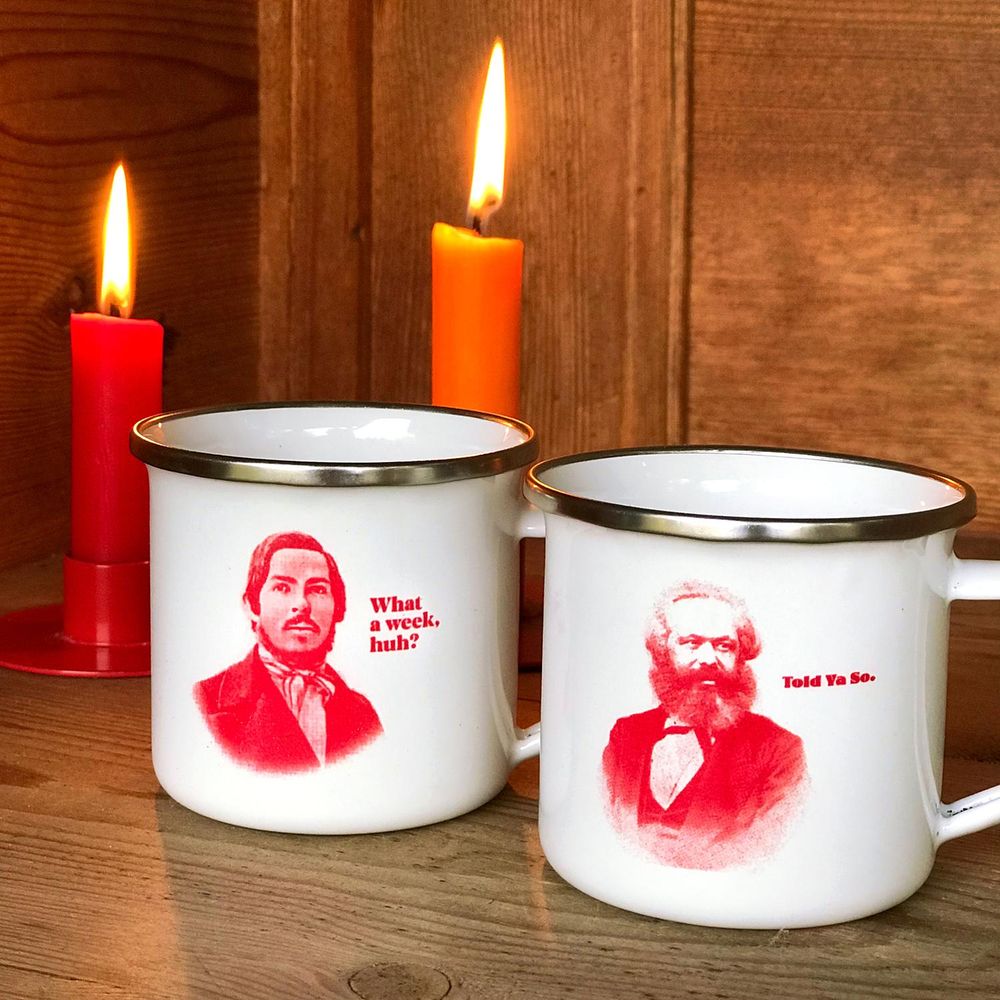 Im Kerzenlicht stehen zwei Emailletassen, die mit dem Porträt von Friedrich Engels und von Karl Marx bedruckt sind. Neben Engels steht: What a week, huh?. Neben Marx: Told Ya So.