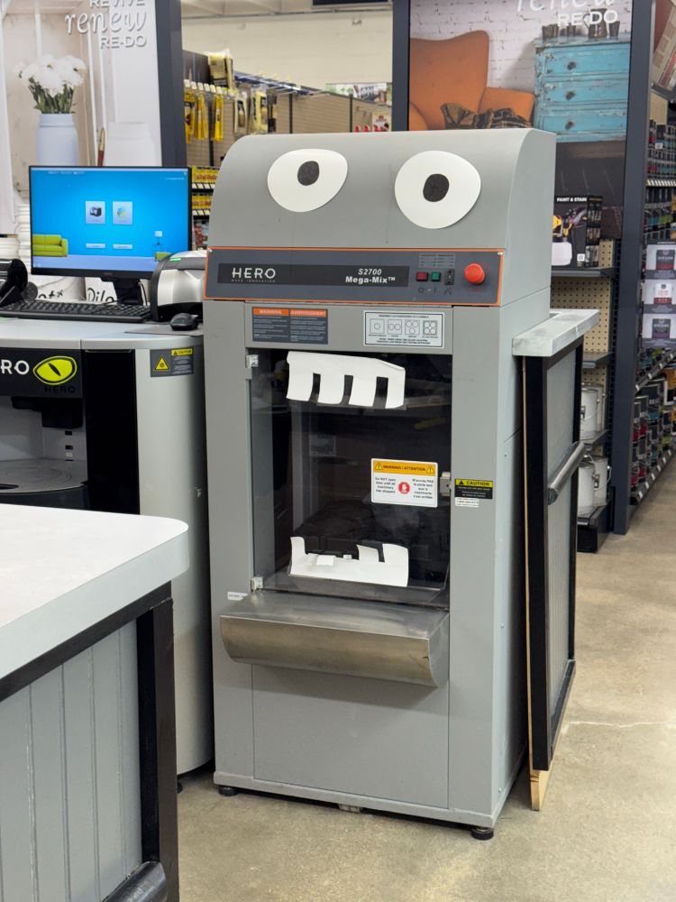 A paint shaking machine at a hardware store with paper teeth and eyeballs added to it to make it look like a monster. 