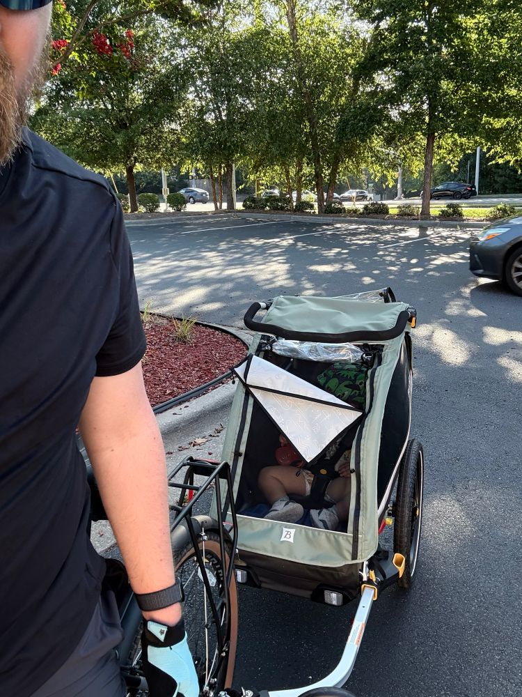 A kinda-selfie showing a baby trailer hooked to a bike in a parking lot