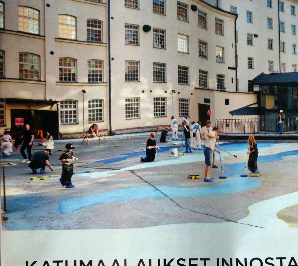 Ihmisiä maalaamassa Finlayson Art Arean sinivalkoisia raitoja pihaan Kuusvooninkisen takana. Tapahtumalehden kuva. 