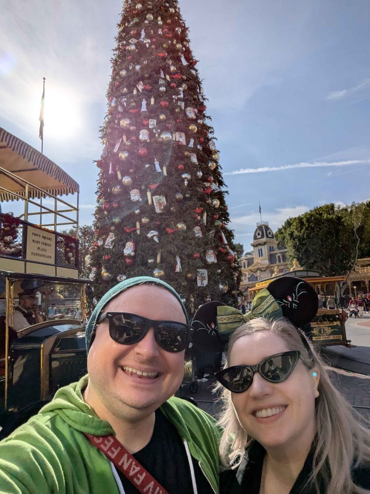 Two people smiling in front of the Disneyland Christmas tree