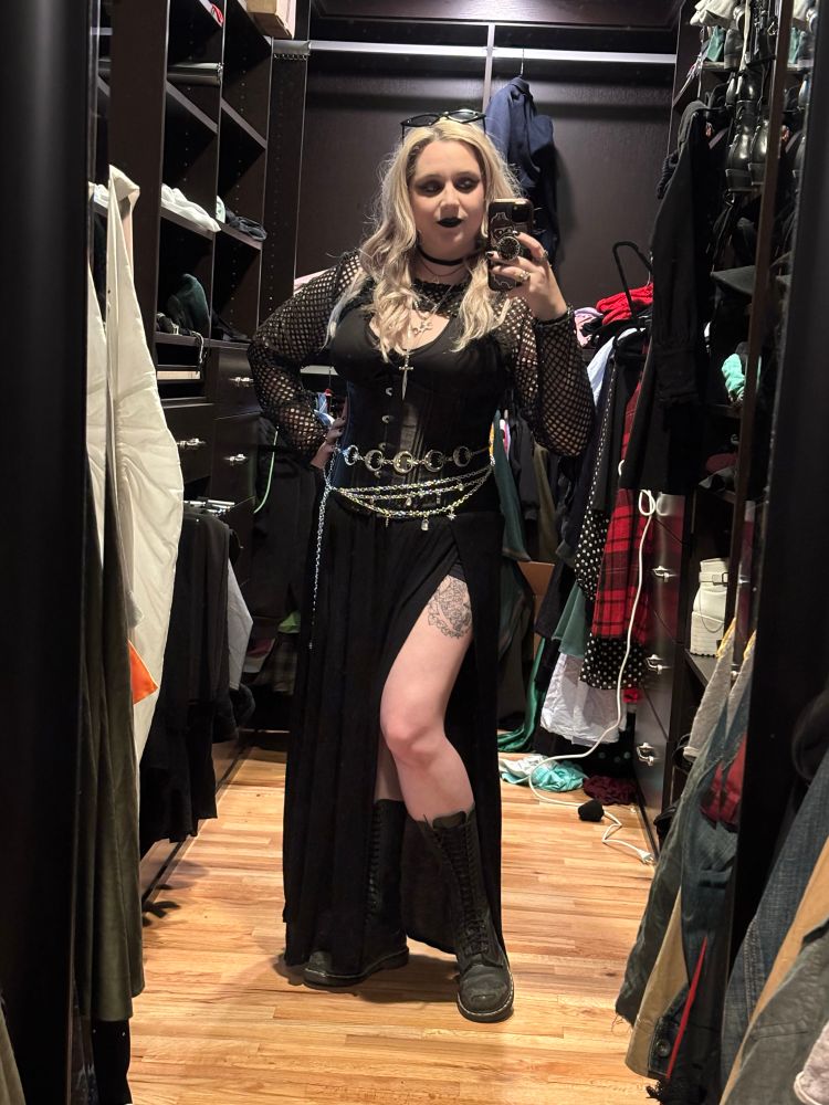 White blonde woman in all black goth outfit in a closet. 