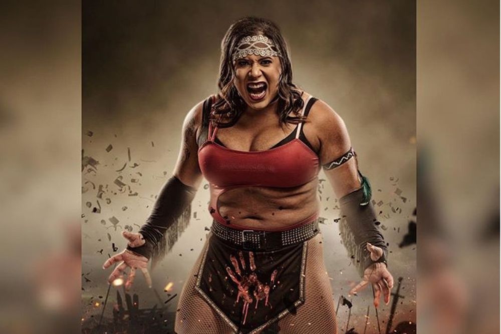 AEW pro wrestler Nyla Rose wearing a red sports bra and dark loincloth with a hand print on it. Roaring whole wearing a patterned headband