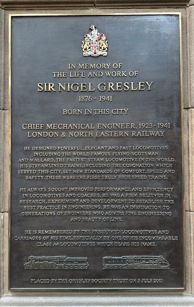 Plaque which reads:
IN MEMORY OF
THE LIFE AND WORK OF
SIR NIGEL GRESLEY
1876 - 1941
BORN IN THIS CITY
CHIEF MECHANICAL ENGINEER, 1923 - 1941
LONDON & NORTH EASTERN RAILWAY
HE DESIGNED POWERFUL, ELEGANT AND FAST LOCOMOTIVES INCLUDING THE WORLD FAMOUS FLYING SCOTSMAN AND MALLARD, THE FASTEST STEAM LOCOMOTIVE IN THE WORLD.
HIS STREAMLINED TRAINS, INCLUDING THE CORONATION WHICH SERVED THIS CITY, SET NEW STANDARDS OF COMFORT, SPEED AND SAFETY. THESE WERE THE FIRST TRULY HIGI SPEED TRAINS.
HE ALWAYS SOUGHT IMPROVED PERFORMANCE AND BEFICIENCY IN LOCOMOTIVES AND COACHES. HE WAS A FIRM BELIEVER IN RESEARCH, EXPERIMENT AND DEVELOPMENT TO ESTABLIST THE BEST PRACTICE IN ENGINEERING. HE WAS AN INSPIRATION TO GENERATIONS OF ENGINEERS WIIO ADMIRE FINE ENGINEERING AND BEAUTY OF LINE.
HE IS REMEMBERED BY THE PRESERVED LOCOMOTIVES AND CARRIAGES OF HIS TIME, ESPECIALLY BY ONE OF TIS INCOMPARABLE CLASS A4 LOCOMOTIVES WHICH BEARS HIS NAME.