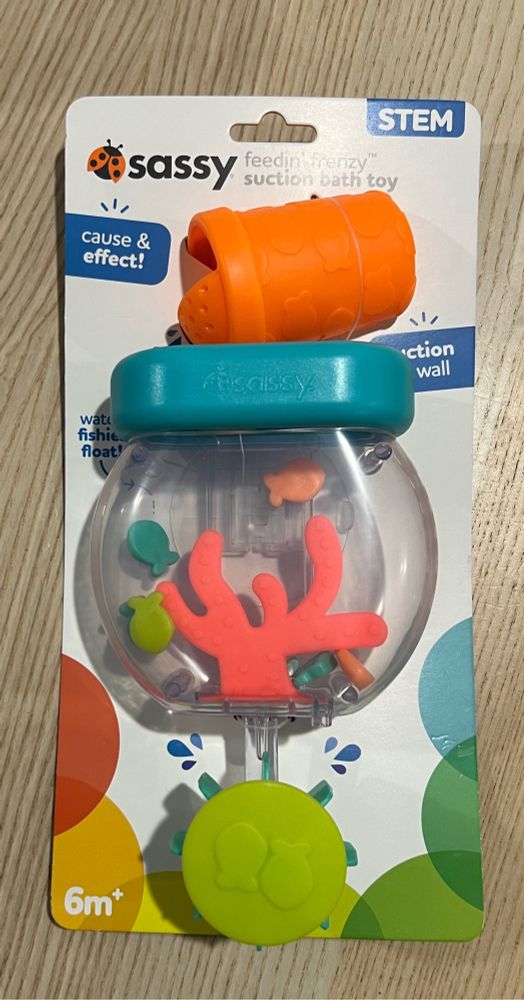 Photo of a bath toy. You pour water in at the top, it fills a fish tank where plastic fish float, and the water streams out of a hole in bottom that spins a wheel.