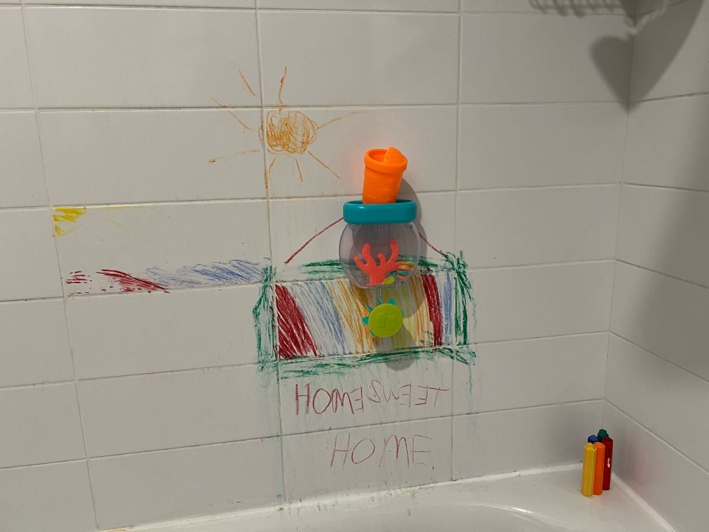 A photo of aforementioned toy suctioned to the bathtub wall. It also has some colorful drawings made by yours truly during a previous bath. You can also see the crayons used in the lower right corner of the photo  