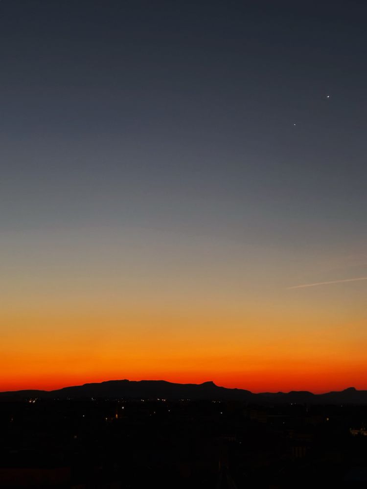 To the top right is Venus (brightest) and Jupiter.

The sunrise over Marseille has produced a clear sky, with a golden glow on the distant horizon.

In the foreground, the city remains in darkness.