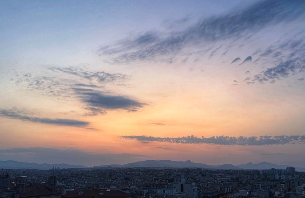 Sunrise view over Marseille. Changing colours in the sky overhead. Grey to blue, with an orange glow.  In the foreground, the buildings are gradually coming out of the darkness.