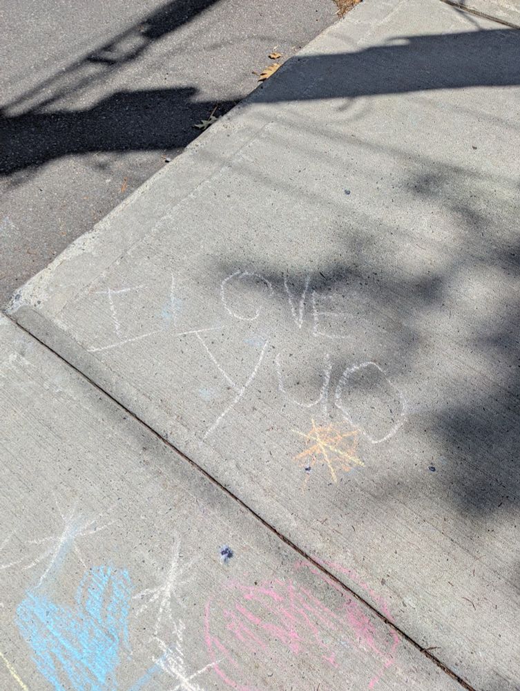 Photo of chalk scribbles on a sidewalk with "I love yuo (sic)" written