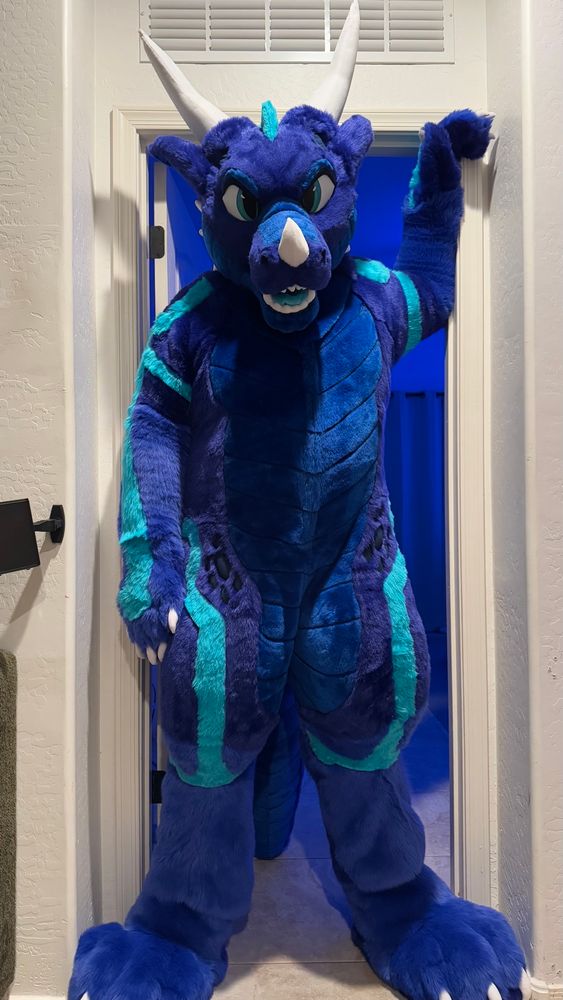 A tall blue dragon fursuiter standing in the doorway. He is taller than the doorframe.