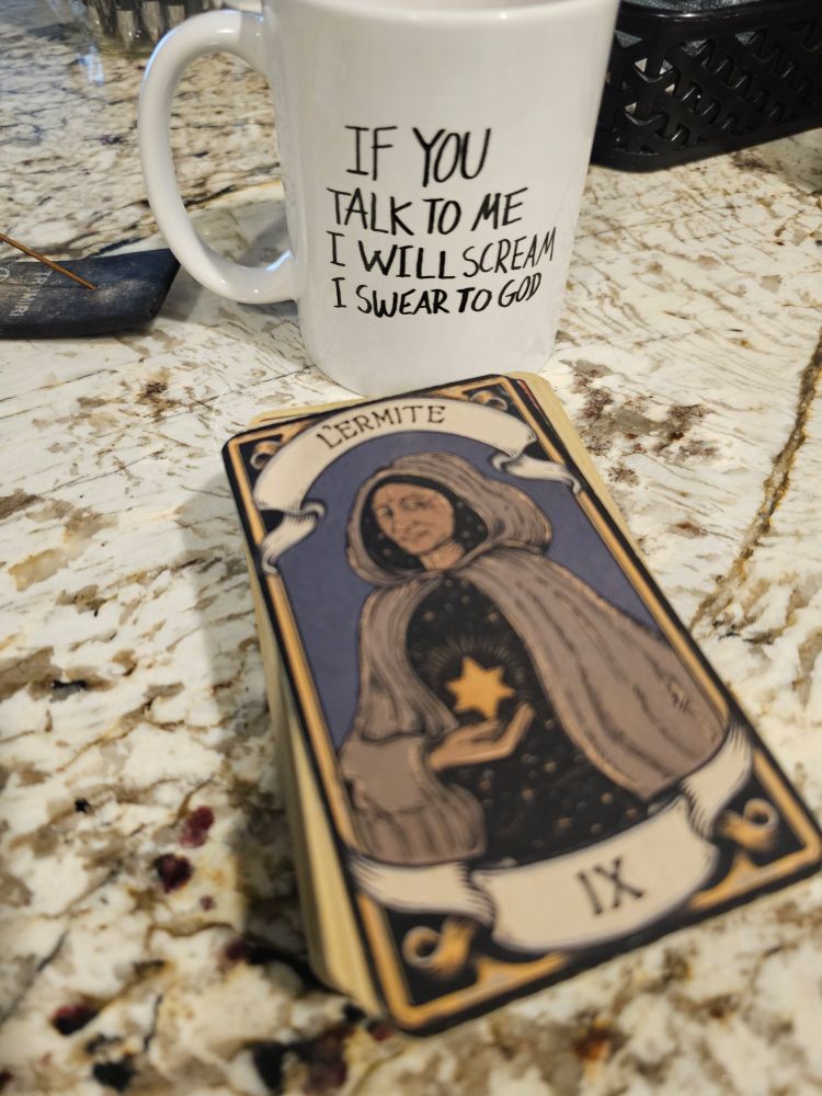 A coffee mug that says "if you talk to me I will scream I swear to god" and a tarot card in French that says "l'ermite"