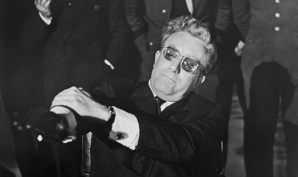 Peter Sellers as Dr. Strangelove in the eponymous Stanley Kubrick film, with his left arm holding his right arm down to prevent it from spontaneously rising into the outstretched, palm-down diagonal position of the Nazi-associated Seig Heil salute.