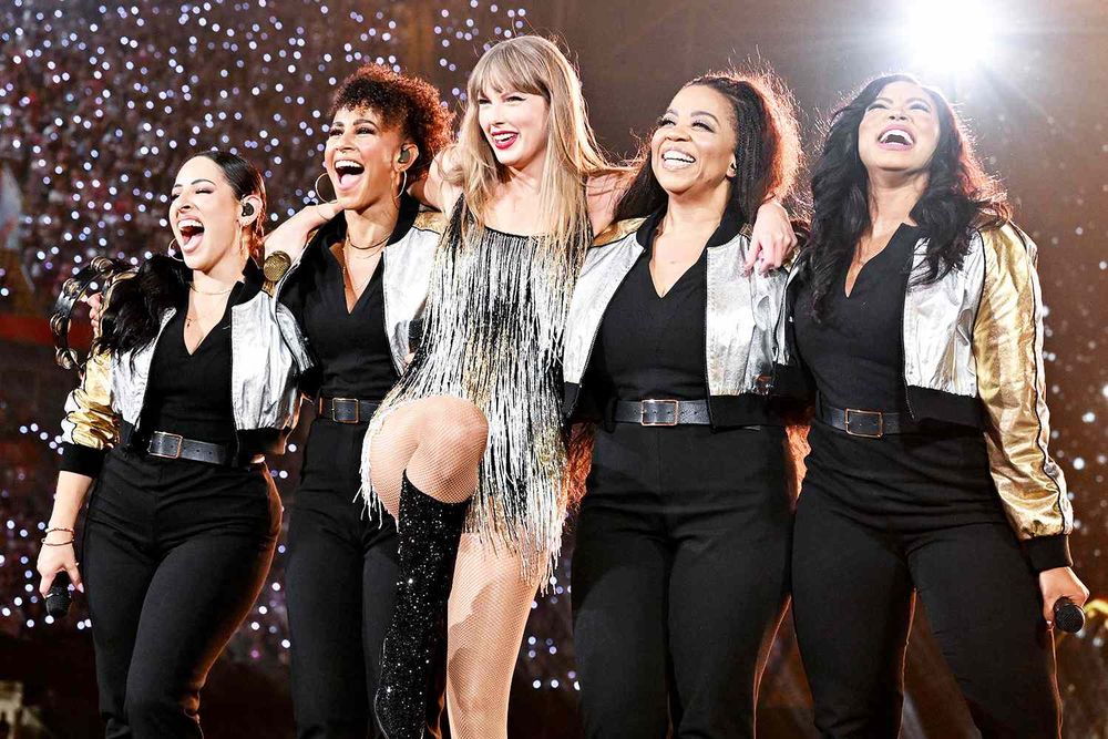 Taylor Swift and her backup vocalist called the Starlights. Taylor is wearing a fringe golden black short dress and boots and the starlight are wearing black with gold and silver jackets. Photo was taken from the fearless set of the Eras tour, 2023-2024