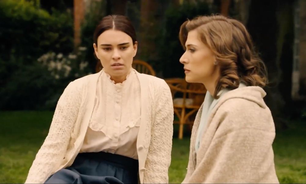 Fina in their garden, wearing white blouse and wool sweather along with a long dark blue dress. She is sitting next to Marta.