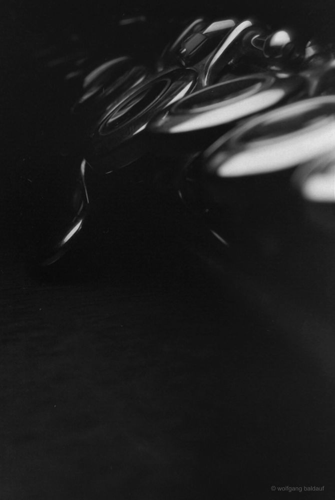This close-up, black and white analog photograph captures the intricate details of a flute. The smooth, metallic surface reflects light, creating highlights and shadows that emphasize the instrument's elegant curves and key mechanisms. The shallow depth of field blurs the background, drawing focus to the flute's craftsmanship.