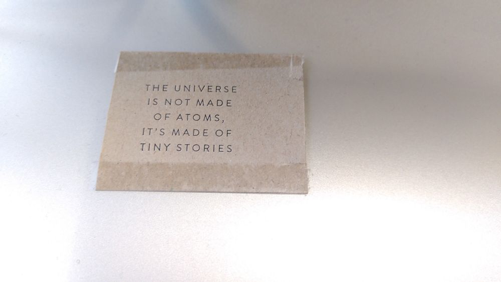 Small piece of beige cardboard with the words 'the universe is not made of atoms, it's made of tiny stories', on a silver background 