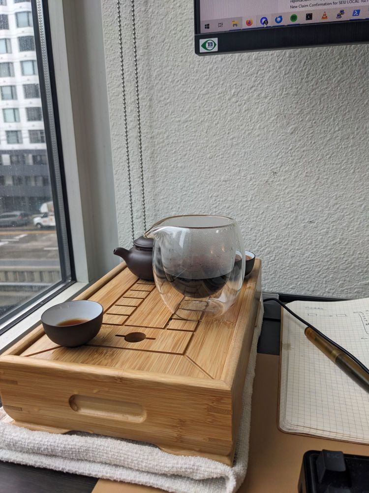 A photo of a bamboo tea tray with a yxing clay pot, decanter and two small tea cups. Dark tea is in the decanter.
