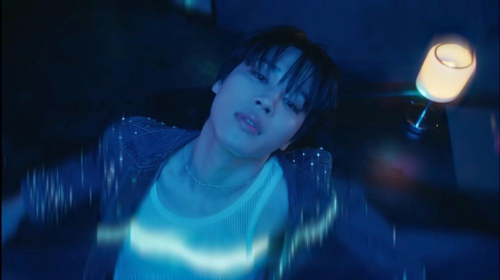 Screenshot of Jimin from the Like Crazy MV. Jimin is leaning back against a bar looking dazed as lights flash over him.