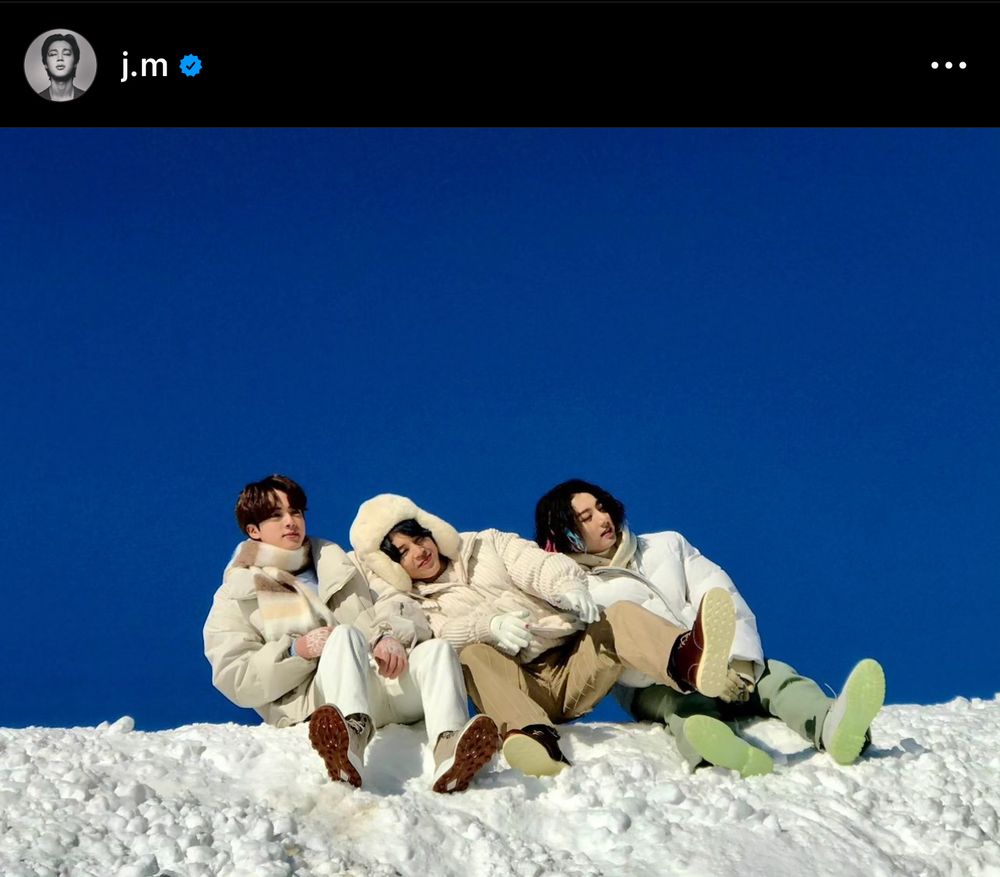 Jin, Jimin and Jungkook sitting on the snow with a clear blue sky behind them.