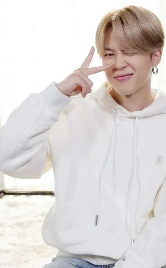 Blond Jimin in a white hoodie, making a peace sign by his eye.