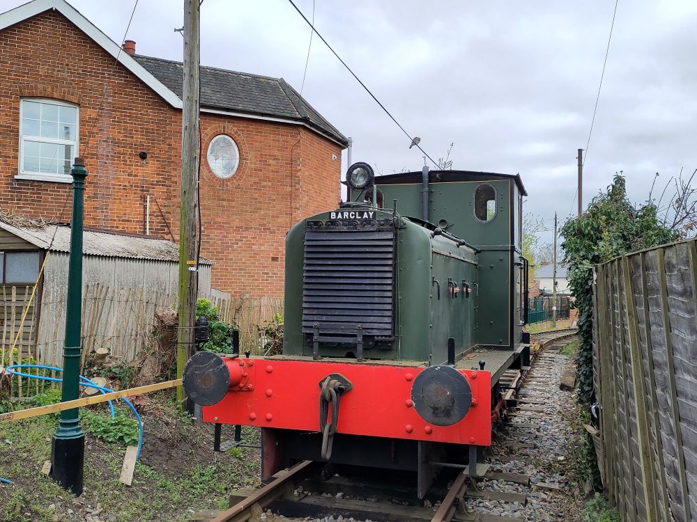 An old shunter loco, parked on a stretch of preserved branch line, between a house and a fence.