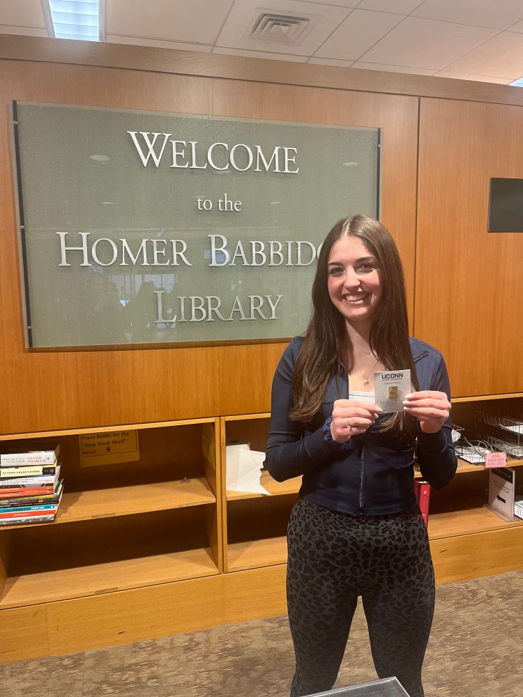 Maria Brennan standing in front of a sign that says Homer Babbidge Library