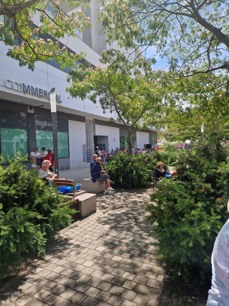 Photo d'un petit coin arboré avec sièges dans une zone piétonne. Des personnes mangent