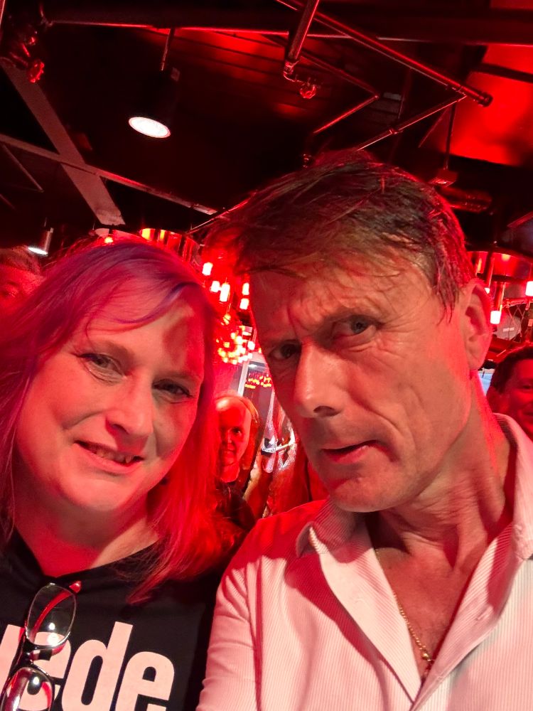 The author posing for a photo with Brett Anderson of Suede. Her husband peeks from behind her in the background.