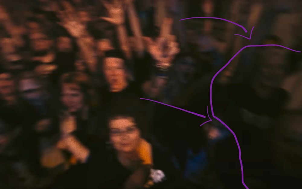 Very blurry, dark image of the crowd at the Suede Dancing With the Europeans video shoot. Arrows point to barely visible and Shawndra and Simon. 