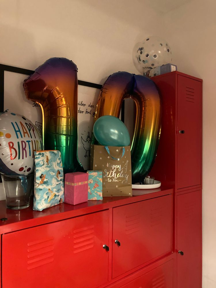 Ein Geburtstagsboard. Rote Blechschränke, auf denen Regenbogenzahlen stehen und einen 10. Geburtstag anzeigen. Ballons und Geschenke.