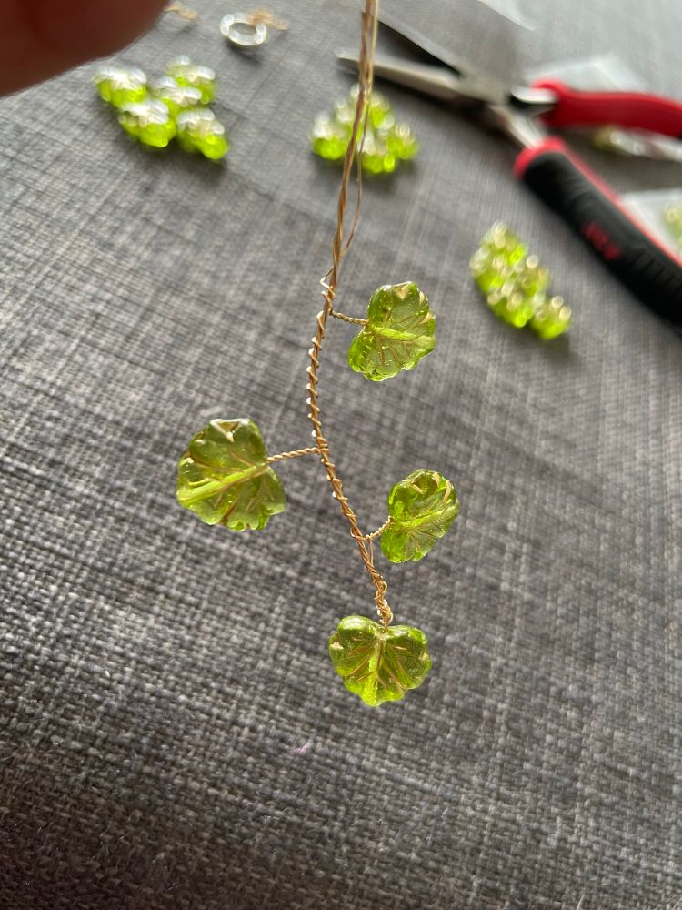 A picture of a 4 glass beads made to look like leaves wire wrapped to create the beginnings of a branch.