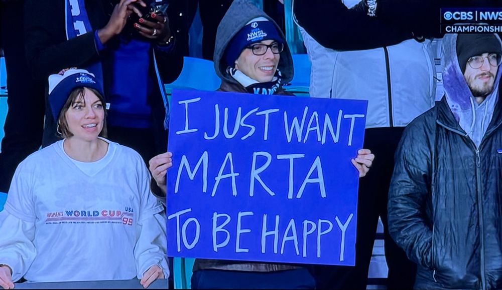 A fan holding a sign that says “I JUST WANT MARTA TO BE HAPPY”