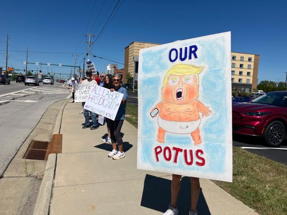 People holding protest signs. Says, Our POTUS with drawing of baby Trump.