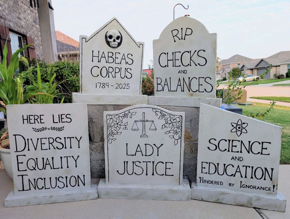 Fake tombstones with RIP CHECKS AND BALANCES, HABEAS CORPUS 1789-2025, HERE LIES DIVERSITY EQUALITY INCLUSION, LADY JUSTICE and SCIENCE AND EDUCATION HINDERED BY IGNORANCE written on them.