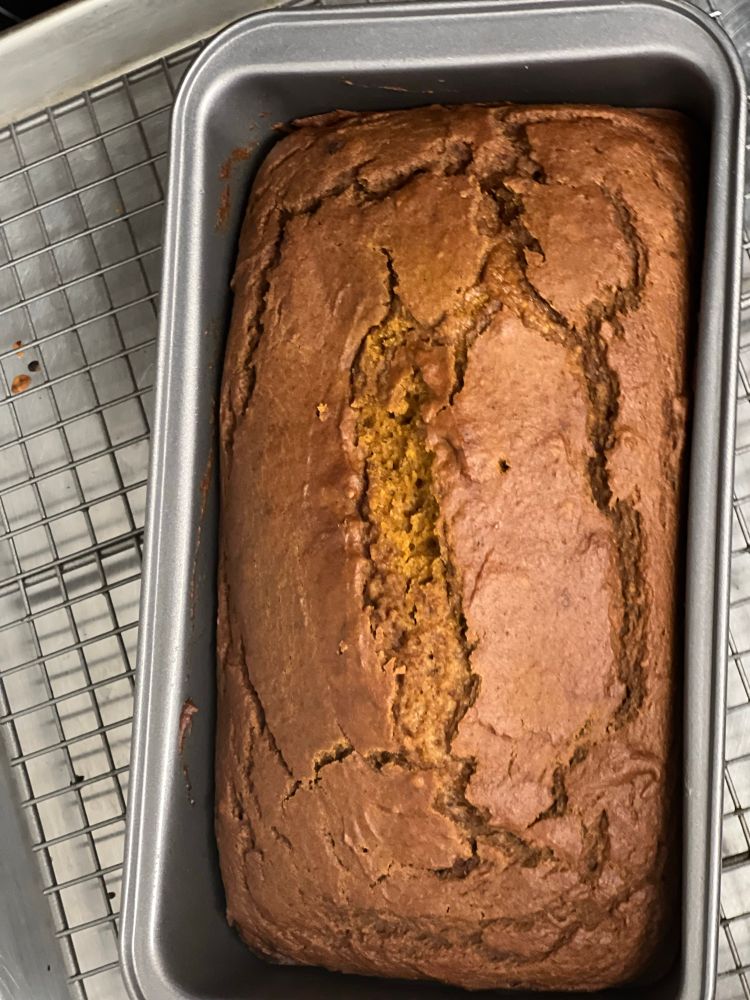 A homemade loaf of pumpkin bread cooling in the pan on a baking rack. 