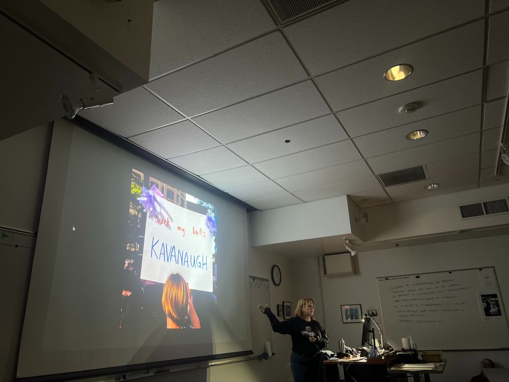Artist Ann-Marie Stillion discussing light and meaning at her residency at Shoreline College, Feb. 10, 2024. This image from the protest on Roe V Wade June 22, 2022 at the Federal building, Seattle. The plaza was darkening at dusk was approaching. Suddenly a beam of light shot between the buildings and bounced behind us. I turned and captured this moment. "Suck My Balls, Kavanaugh." @Artists Rights Society, NY.