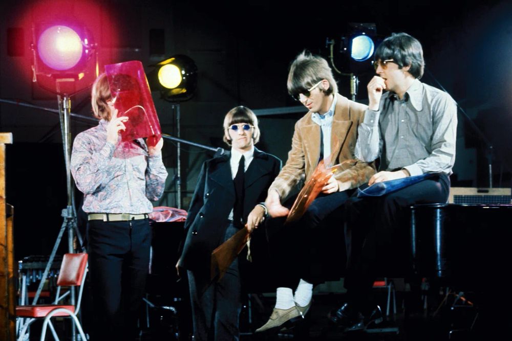 John Lennon tries to hide behind a piece of see-through pink plastic, not understanding Ringo, George and Paul can still see him. 