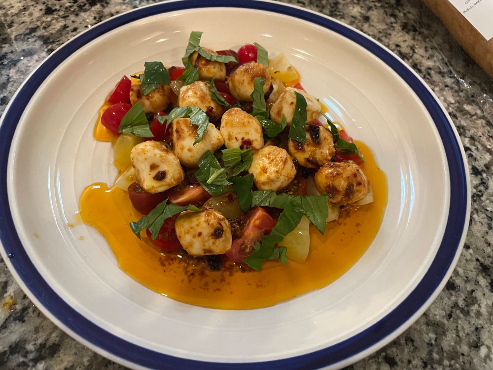Photo of a meal. Chili crisp marinated mozzarella balls are on top of tomatoes topped with some fresh basil. 